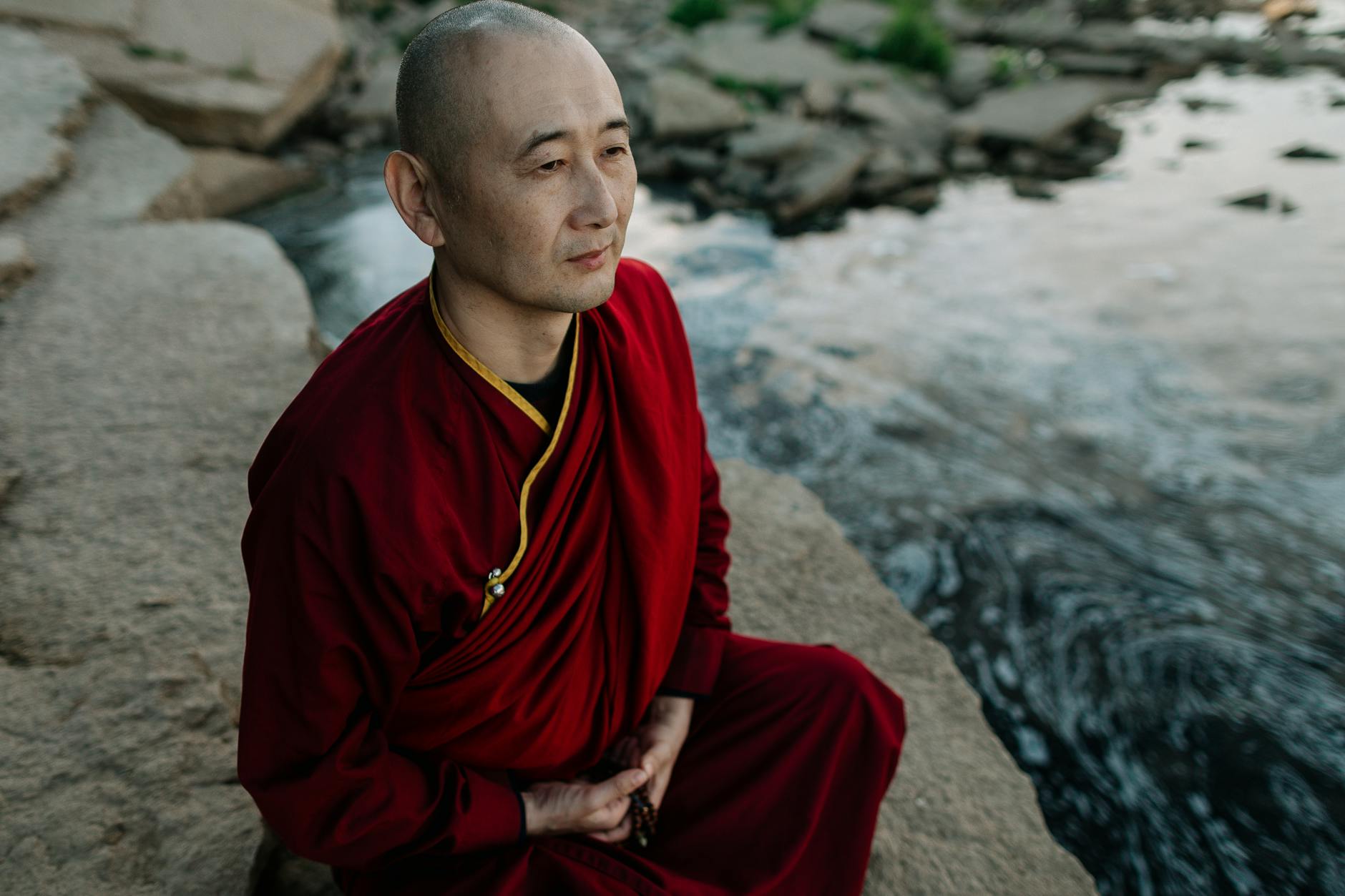 meditating tibetan monk sitting on the rocky riverbank