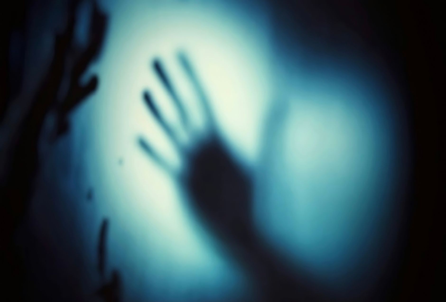 A blurred shadow of a hand pressed against a surface, with a blue-toned background.