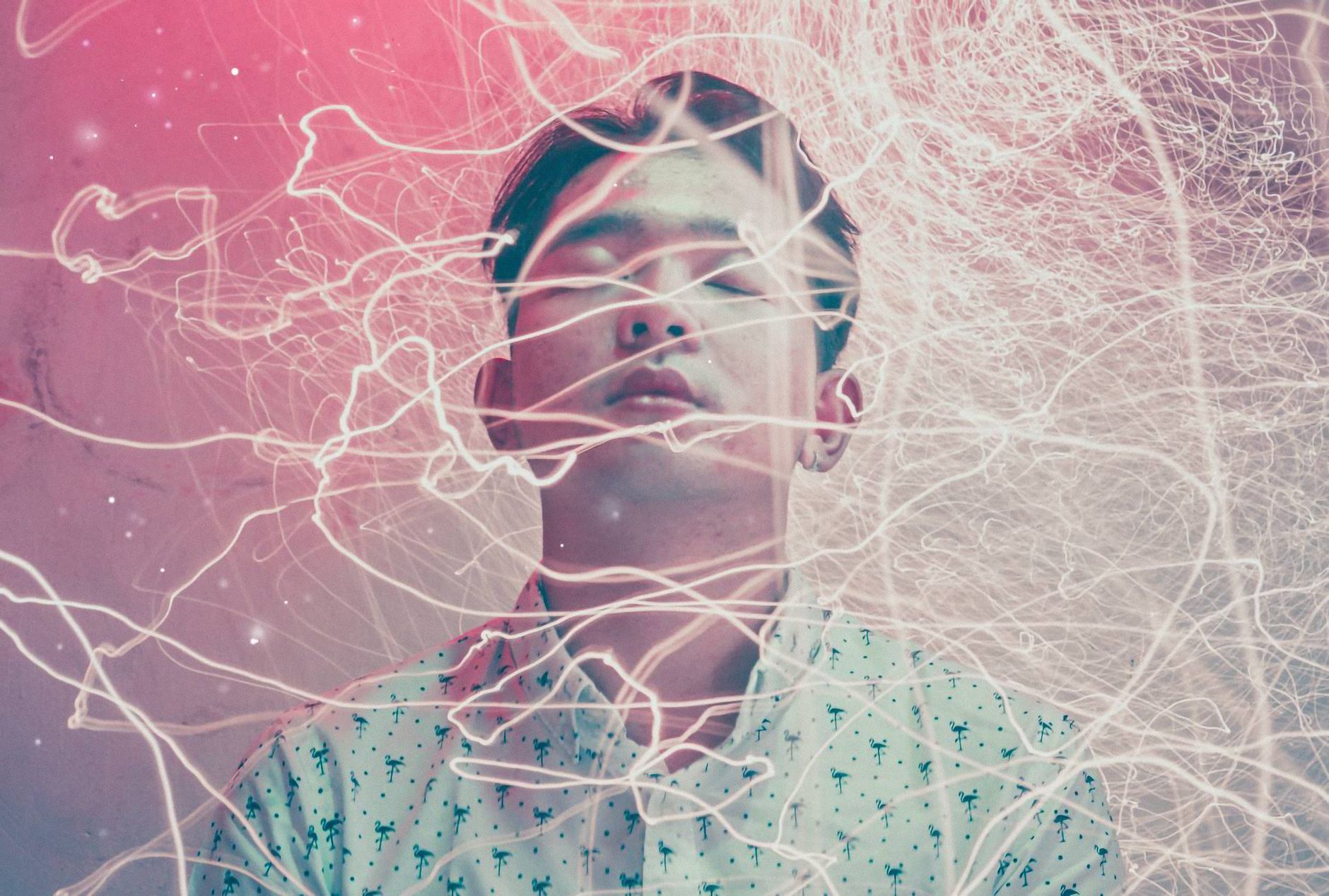 A person with closed eyes is surrounded by swirling light trails and abstract patterns, creating a dreamy and ethereal atmosphere.